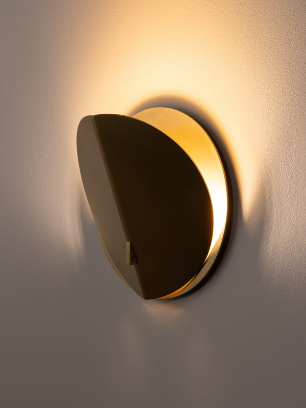 Folded wall sconce shown in natural brass finish, side angle, illuminated