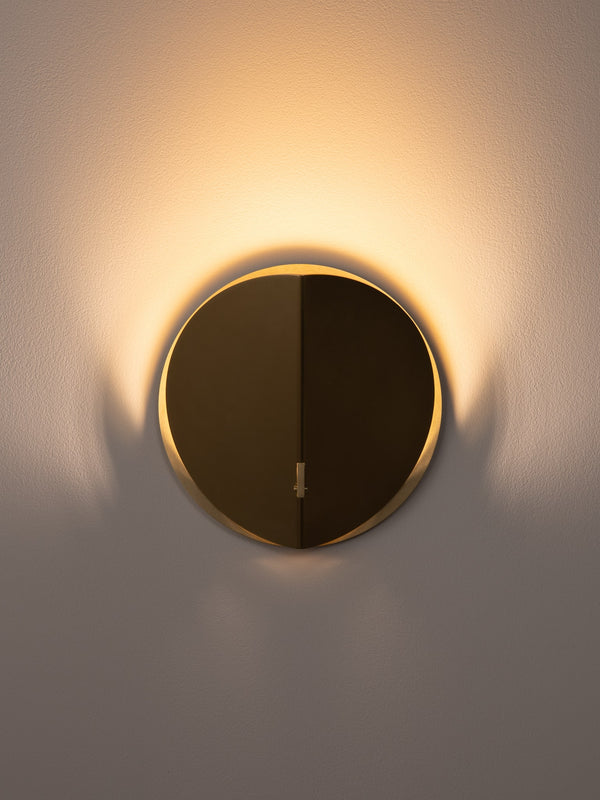 Folded wall sconce shown in natural brass finish, front view, illuminated