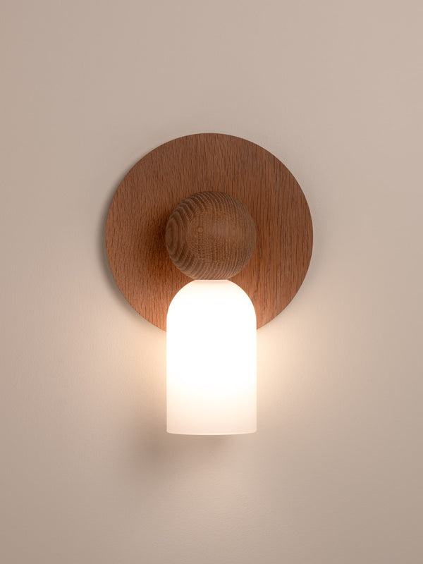 Libby wall sconce shown in natural oak finish, front view, illuminated