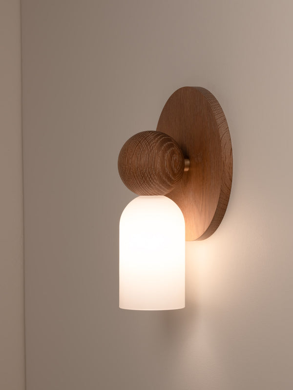 Libby wall sconce shown in natural oak finish, side angle, illuminated