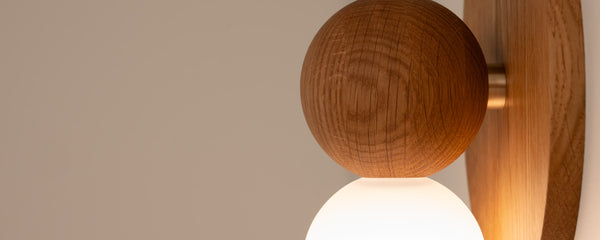 Libby wall sconce shown in warm oak finish, zoomed in to detail of wood grain and natural brass connector
